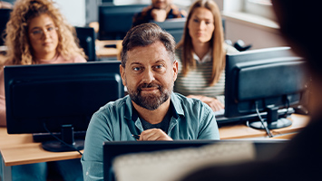A group of adults in a computer lab listening to their instructor.