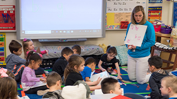 A Kindergarten class sitting on the floor engaged in a dictation activity.