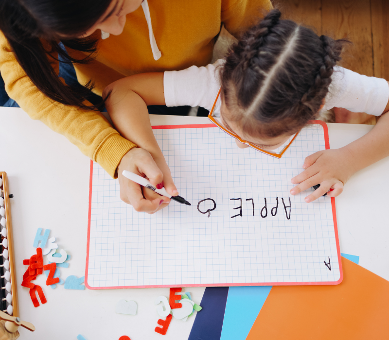 Teacher and student writing the word "apple".
